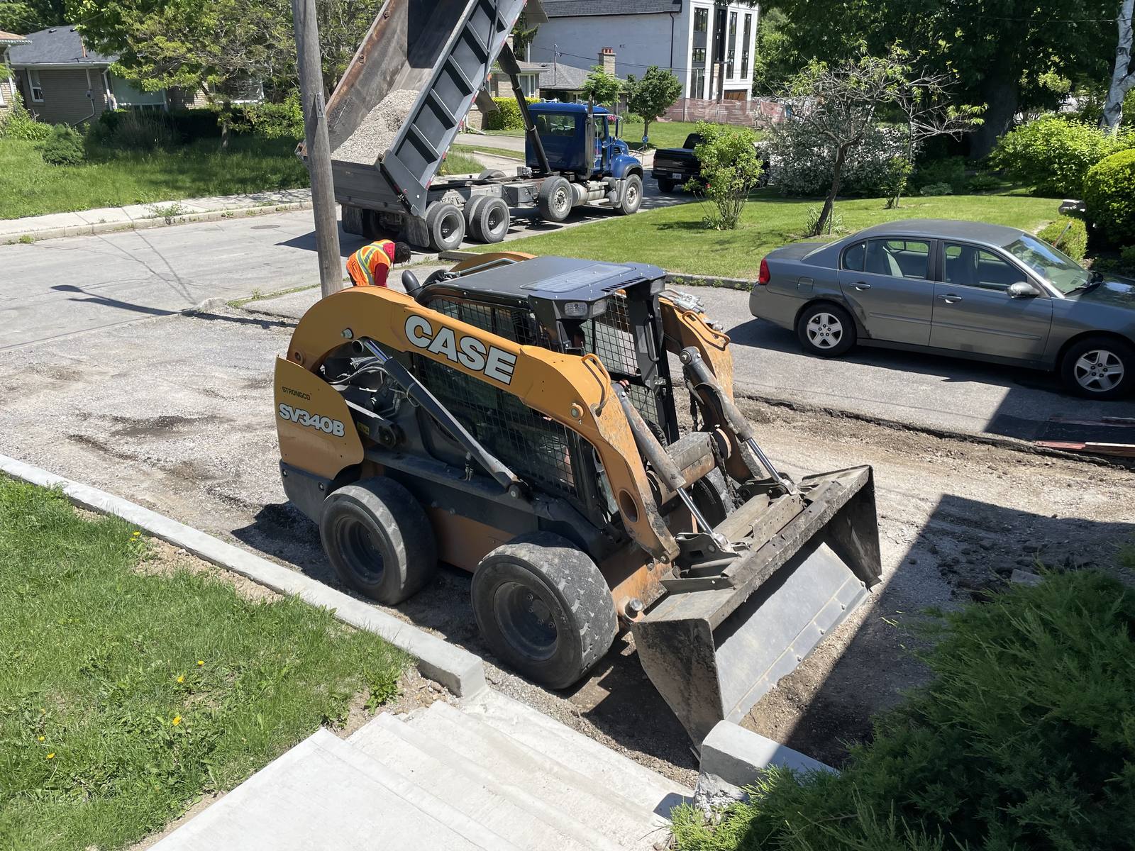 Driveway reconstruction — skid steer and dump truck placing crushed stone base behind new concrete curbing — Berm Inc.