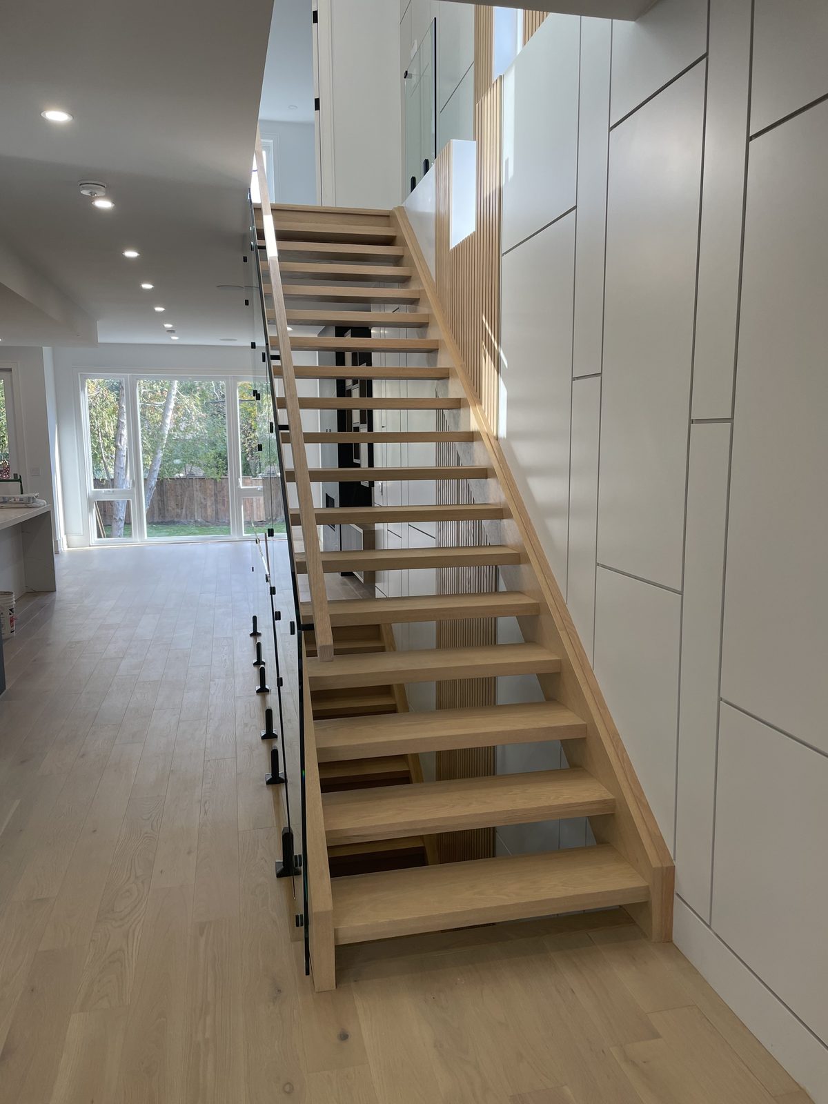 Open-riser oak staircase with glass railing — Berm Inc. project photo