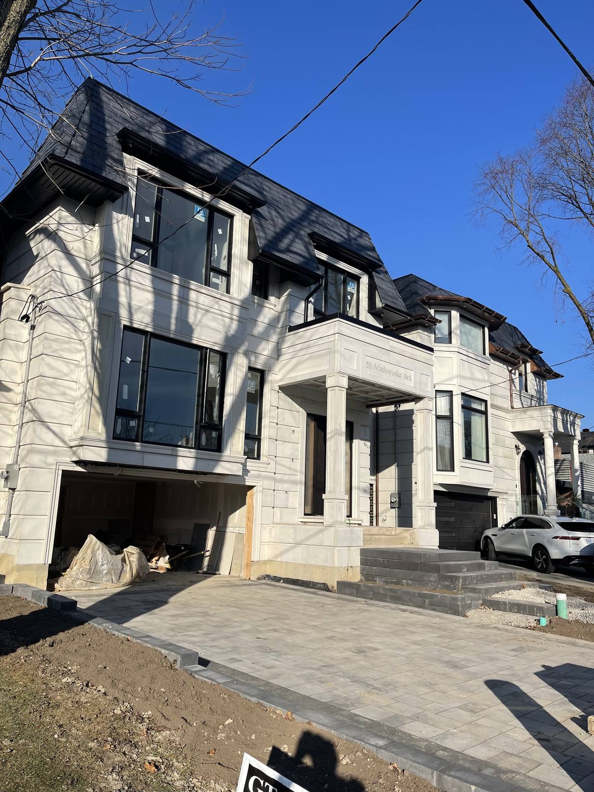 Custom home nearing completion — stone cladding, black-framed windows and interlocking stone driveway — Berm Inc.