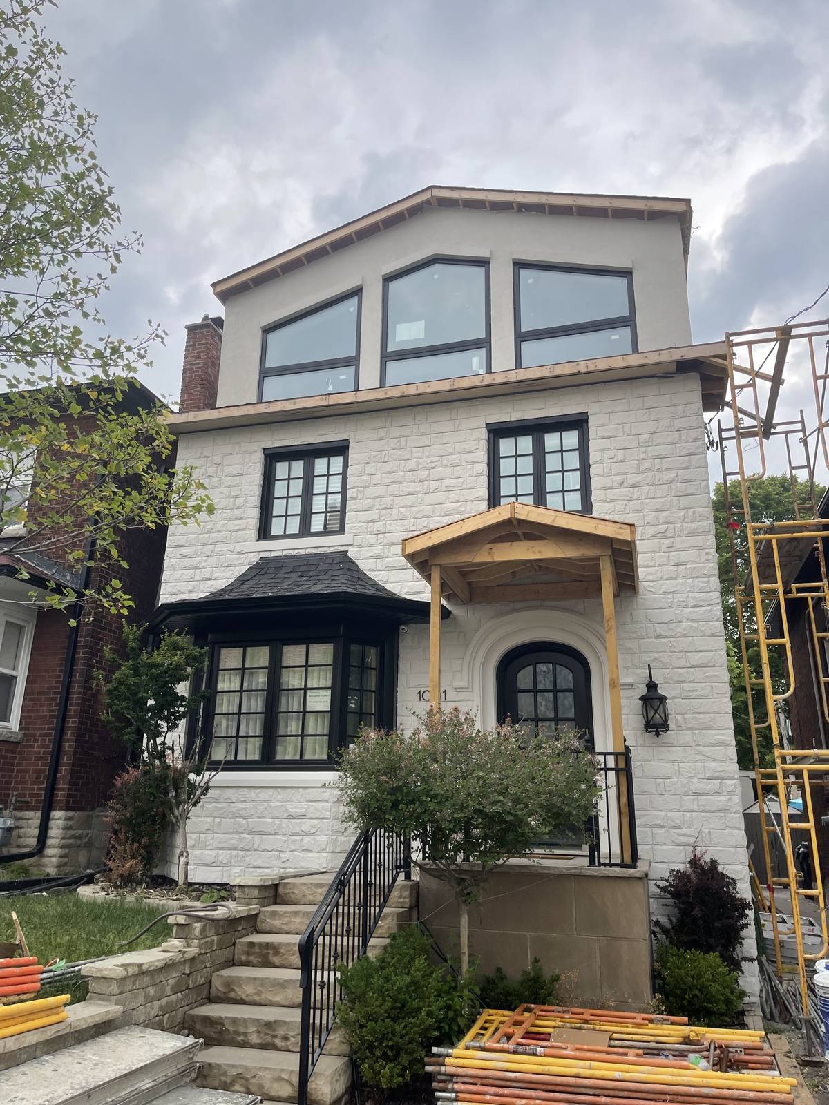 Second-storey addition under construction by Berm Inc. — masonry-clad home with scaffolding and framing in progress